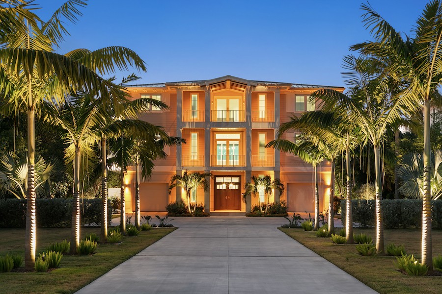 A mansion surrounded by palm trees, all of which are illuminated by outdoor lights.