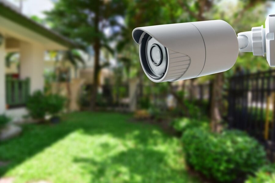 A surveillance security camera in the foreground with a backyard in the background.