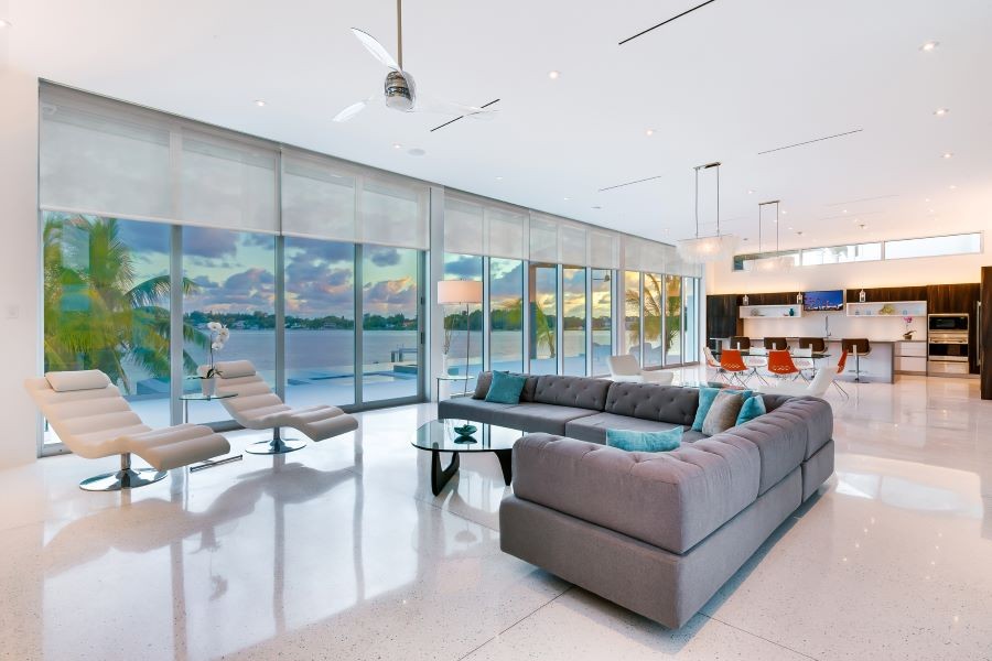 A modern home with an open floor plan and a row of windows with motorized shades partially drawn overlooking the ocean. 