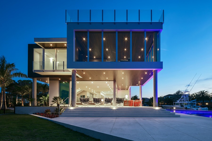 A contemporary home on the coast at night with large windows and DMF lighting on the interior.