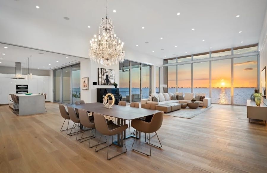 A home with an open floor plan illuminated by various fixtures overlooking the sun setting into the ocean.